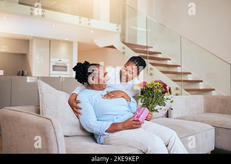 Fête des mères, femme noire et fleurs surprise sur le canapé pour cadeau, boîte ou cadeau à maman dans le salon. Femme, bouquet ou mama senior sur un canapé avec wow Banque D'Images