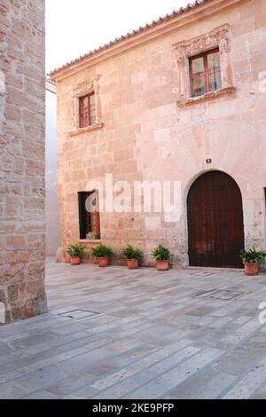 Ancien mur en pierre avec porte en bois et fleurs en pot à côté d'une rue dans la vieille ville d'Alcudia, Majorque, Espagne. Banque D'Images