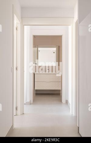 Couloir lumineux avec murs blancs et sol carrelé avec porte donnant sur la salle de bains Banque D'Images