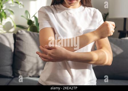 Gros plan d'une jeune femme souffrant de douleurs au bras. Malsain fille caucasienne souffrant de douleurs au coude et de massing main douloureuse assise sur le canapé à la maison. Femme Banque D'Images