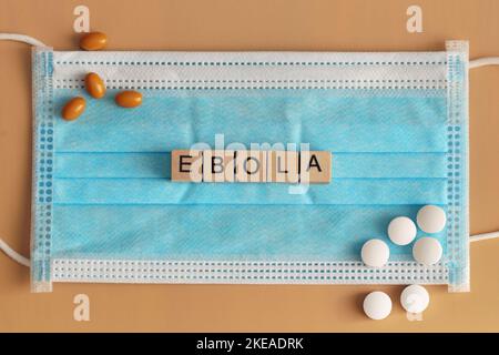Ebola est disposé avec des cubes en bois sur un masque chirurgical. Il y a plusieurs pilules qui traînent autour. Fièvre hémorragique virale. Banque D'Images