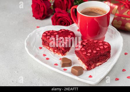 Gâteaux velours rouge en forme de coeur sur plaque blanche, roses, cadeaux et tasse de café pour la Saint Valentin sur fond gris clair Banque D'Images