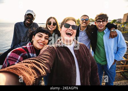 Groupe d'amis multiethniques heureux moment bord de mer - heureux groupe d'amis divers appréciant une belle journée ensoleillée prenant le portrait de smartphone selfies a Banque D'Images