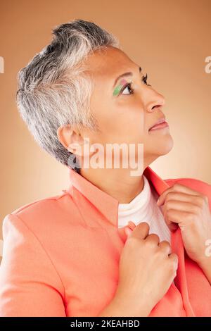 Penser, mode et femme âgée avec maquillage, style designer et élégant avec des vêtements sur un fond brun studio. Cosmétiques, visage et personnes âgées Banque D'Images