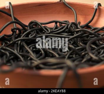 Un bol en bois désordonné de spaghetti de seiches noires sur une surface en tissu chaud - rendu 3D Banque D'Images