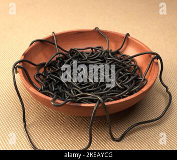 Un bol en bois désordonné de spaghetti de seiches noires sur une surface en tissu chaud - rendu 3D Banque D'Images