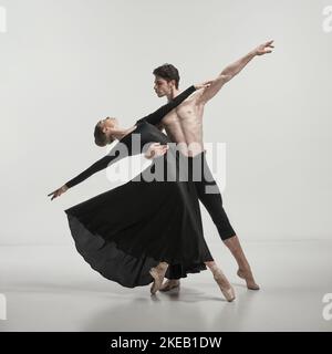 Jeune homme musclé et femme en robe de soie noire, danseurs de ballet se exécutant isolé sur fond gris studio Banque D'Images