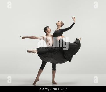 Jeune homme musclé et femme en robe de soie noire, danseurs de ballet se exécutant isolé sur fond gris studio Banque D'Images