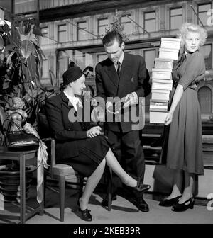 Magasin de chaussures en 1940s. Une femme dans le shoestore de Hamngatan Stockholm 1948. Elle est parfaitement entretenue avec un vendeur montrant un modèle de chaussure à la mode, et une assistante féminine avec des boîtes de chaussures prêtes à être essayées. Suède 1948. Conard réf. 957 Banque D'Images