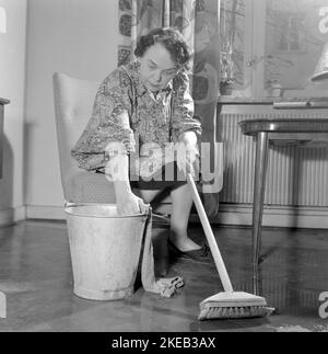 Nettoyer le plancher à l'arrière. Une femme semble très fatiguée et usée lorsqu'elle est assise sur une chaise, ayant un repos dans le travail de nettoyage des sols. Suède 1956 Conard réf. 3160 Banque D'Images