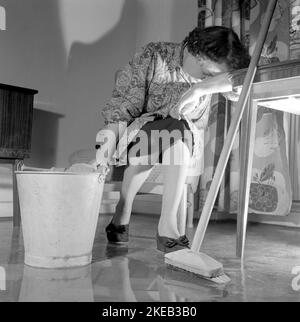 Nettoyer le plancher à l'arrière. Une femme semble très fatiguée et usée lorsqu'elle est assise sur une chaise, ayant un repos dans le travail de nettoyage des sols. Suède 1956 Conard réf. 3160 Banque D'Images