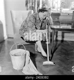 Nettoyer le plancher à l'arrière. Une femme semble très fatiguée et usée lorsqu'elle est assise sur une chaise, ayant un repos dans le travail de nettoyage des sols. Suède 1956 Conard réf. 3160 Banque D'Images