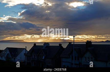 Une vue sur les toits au soleil couchant avec des rayons crépusculaires sur l'île de Rum à l'horizon sur la côte ouest de Mallaig, Morar, Écosse. Banque D'Images