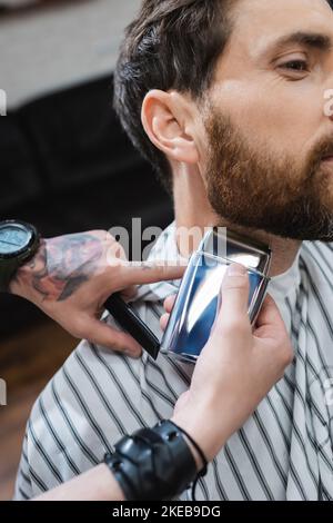 vue rognée du cou de rasage barber de l'homme barbu avec rasoir électrique, image de stock Banque D'Images