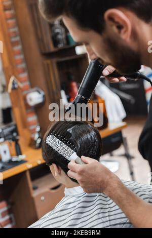 Coiffeur flou peignant et sécher les cheveux de l'adolescent garçon dans le salon de beauté, image de stock Banque D'Images