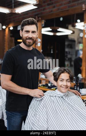 coiffeur souriant et adolescent regardant la caméra dans le barbershop, image de stock Banque D'Images