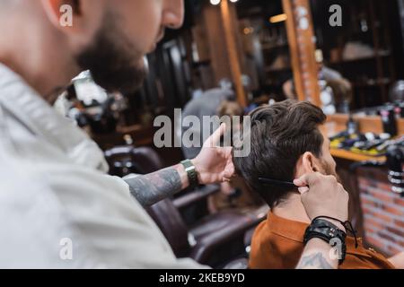 barber tatoué flou peignant les cheveux de l'homme dans barbershop, image de stock Banque D'Images