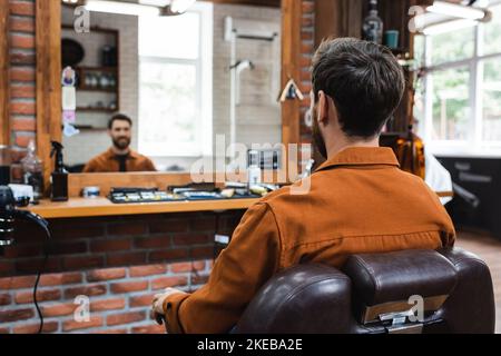 vue arrière de l'homme de brunette assis dans la chaise de coiffure près du miroir flou, image de stock Banque D'Images