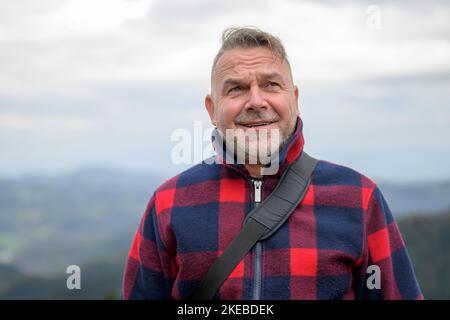 Un homme d'âge moyen aux cheveux gris avec une barbe et une veste de bûcheron regarde le ciel de manière critique en raison du mauvais temps Banque D'Images