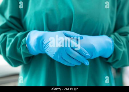 Section médiane de la femme chirurgien prête pour l'opération en gants chirurgicaux bleus et robe verte Banque D'Images