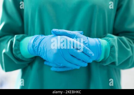 Section médiane de la femme chirurgien prête pour l'opération en gants chirurgicaux bleus et robe verte Banque D'Images