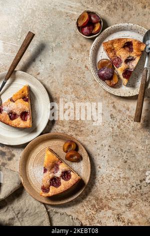 Morceaux de la tarte au gâteau au Plum du New York Times avec sucre en poudre et épices sur fond brun texturé, vue de dessus, plat. Orientation verticale Banque D'Images