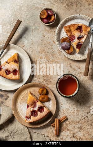 Morceaux de la tarte au gâteau au Plum du New York Times parsemée de sucre en poudre pour le thé sur fond texturé brun, concept de fête de thé d'automne, vue de dessus, fla Banque D'Images