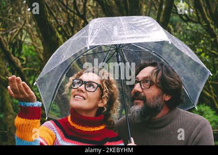 Jeune couple mature homme et femme vérifiant le temps sous parapluie le jour des pluies. Activités de loisirs en plein air personnes dans le parc en automne ou en hiver. Pluie et mauvais état de prévision. Amour et amis Banque D'Images