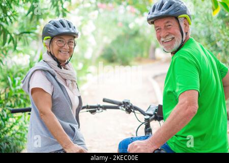 Deux personnes âgées heureux et matures appréciant et faisant du vélo ensemble pour être en forme et en bonne santé à l'extérieur. Les aînés actifs ayant une formation amusante dans la nature. Portrait de deux personnes âgées regardant l'arrière de l'appareil photo Banque D'Images