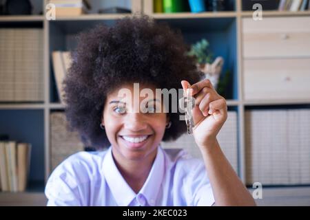 Agent immobilier tenant les clés du nouvel appartement. Portrait d'une jeune femme à la peau sombre et attrayante avec une coiffure afro maurienne tenant de nouvelles clés de maison. Femme africaine américaine propriétaire montrant les clés. Banque D'Images