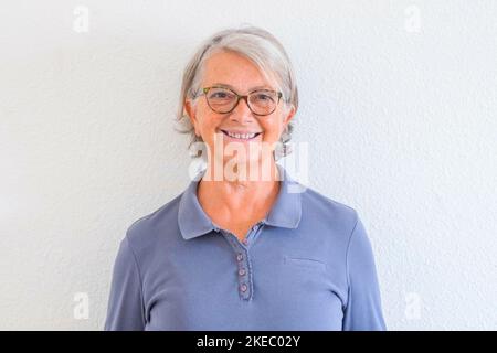 gros plan et potrait de femme mûre souriant et regardant à la caméra avec un mur blanc à l'arrière-plan - concept senior actif et mode de vie Banque D'Images
