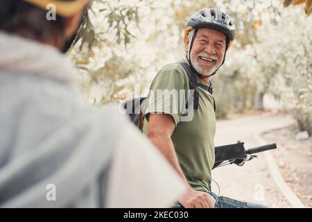 Deux personnes âgées heureux et matures appréciant et faisant du vélo ensemble pour être en forme et en bonne santé à l'extérieur. Les aînés actifs ayant une formation amusante dans la nature. Portrait d'un vieil homme souriant lors d'un voyage en vélo avec sa femme. Femme indiquant quelque chose et la regardant. Banque D'Images