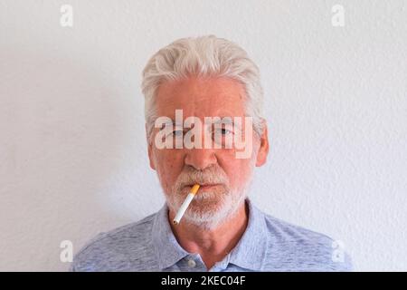 gros plan et portrait de l'homme mature ou retraité senior fumeur et regardant l'appareil photo avec fond blanc - mauvaise décision essayant de s'en sortir Banque D'Images