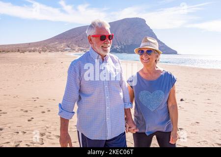 couple de personnes âgées mûres ayant plaisir à marcher sur le sable de la plage ensemble appréciant leurs vacances et vacances ou voyage à l'extérieur avec la mer ou l'océan à l'arrière-plan - deux personnes âgées en amour de s'amuser Banque D'Images