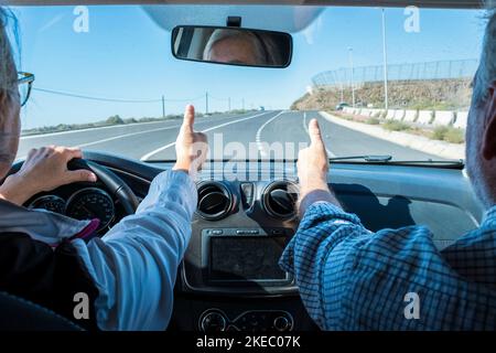 couple d'aînés conduisant et s'amusant avec une voiture de location dans la rue - deux retraités en vacances ensemble - homme et femme avec le doigt de la main vers le haut - oui et concept de conduite sûre Banque D'Images