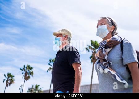 couple de deux personnes âgées ou adultes marchant ensemble à l'extérieur de l'aéroport portant un masque médical pour empêcher tout type du virus comme le coronavirus ou le covid-19 - personnes caucasiennes sûres concept et style de vie Banque D'Images