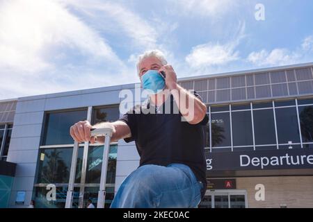 un homme âgé et mature prêt à voyager dans le monde avec une pandémie - retraité dans l'aéroport portant un mak chirurgical et médical pour prévenir la maladie ou covid-19 - appelant et utilisant son téléphone Banque D'Images