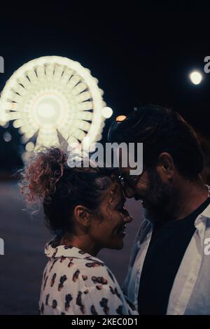 Couple aimant s'embrassant passionnément dans la rue contre la roue lumineuse de ferris la nuit. Couple romantisme et passer du temps de qualité à l'extérieur pendant les vacances la nuit Banque D'Images