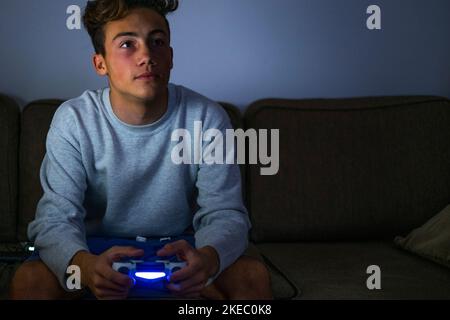 portrait et gros plan d'un adolescent ou d'un millénial jouant de la vidéo jeux avec une manette à la maison tard dans la nuit le canapé - mauvais style de vie malsain de la plupart des parties de garçons Banque D'Images