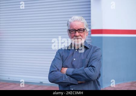 portrait et gros plan d'un vieil homme d'âge mûr regardant l'appareil photo avec à l'arrière son magasin fermé pour le confinement de quarantaine - homme d'affaires professionnel Banque D'Images