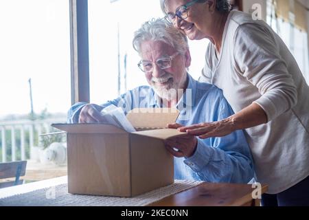 Heureux mûr vieux couple de famille de déballage boîte de carton, satisfait avec l'achat de magasin d'Internet ou cadeau inattendu, se sentant excité de livraison rapide service d'expédition, expérience d'achat positive. Banque D'Images