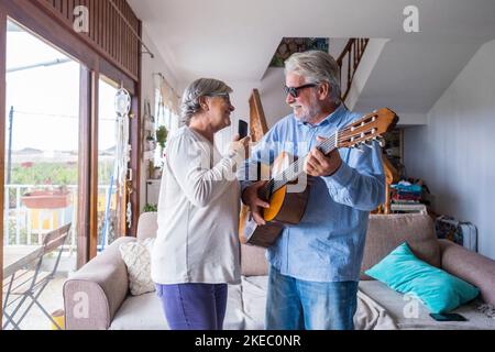 Heureux et drôle couple de personnes âgées et matures ayant le plaisir et appréciant à la maison faisant une fête ensemble chantant et dansant jouant la guitare à l'intérieur. Concept de fête ou d'événement. Banque D'Images