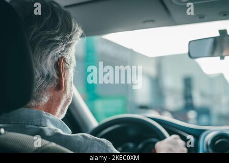 Vue arrière de l'ancien homme à la retraite conduisant dans la rue avec sa voiture. Banque D'Images
