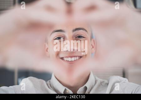 Un adolescent affectueux et joyeux prend un portrait romantique de selfie en regardant l'appareil photo à travers le cœur des doigts joints. Une jeune dame épris tire amour confesser à l'homme aimé sur vidéo le jour de la Saint-Valentin Banque D'Images