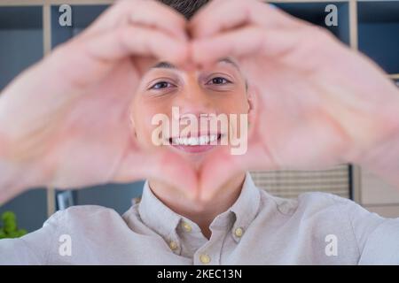 Un adolescent affectueux et joyeux prend un portrait romantique de selfie en regardant l'appareil photo à travers le cœur des doigts joints. Une jeune dame épris tire amour confesser à l'homme aimé sur vidéo le jour de la Saint-Valentin Banque D'Images