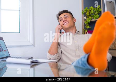 Adolescent satisfait heureux de parler au téléphone au travail avec un ordinateur portable au bureau, lève les mains et met les pieds sur la table, se détendre après une dure journée de travail en prévision d'un congé de fin de semaine, une journée de travail détendue, aucun stress Banque D'Images