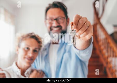 Portrait d'un couple caucasien heureux tenant de nouvelles clés de maison. Une femme et un mari joyeux se sentent heureux d'acheter une nouvelle maison. Les propriétaires de maisons sont fiers de se tenir à l'intérieur et de montrer leurs clés après leur déménagement. Banque D'Images