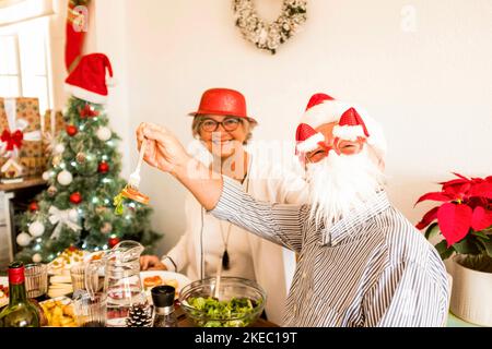 couple de deux personnes âgées et matures appréciant la nourriture et manger à la table de leur maison le jour de noël à l'intérieur - joyeux et heureux adultes retraités Banque D'Images