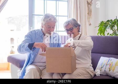 Heureux mûr vieux couple de famille de déballage boîte de carton, satisfait avec l'achat de magasin d'Internet ou cadeau inattendu, se sentant excité de livraison rapide service d'expédition, expérience d'achat positive. Banque D'Images