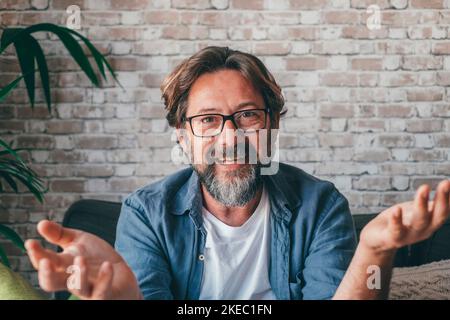 Portrait d'un homme mûr en lunettes de vue en train de gesturer et de parler à l'appareil photo. Joyeux tuteur en ligne de race blanche donnant un cours de formation pédagogique ou faisant un appel de vidéo conférence. Banque D'Images